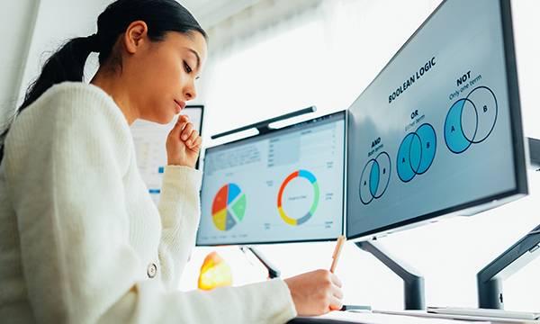 Research terminology and images on two computer screens, as a nursing student sits at a desk studying