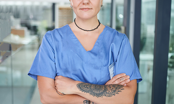 Uniform policy for nursing students: a nurse stands with arms folded showing a large tattoo on her arm