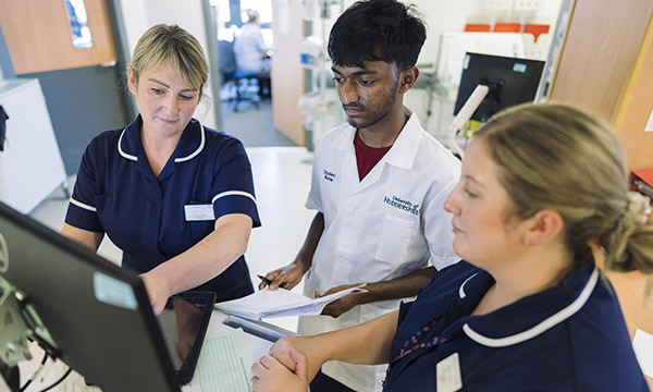 Clinical nurse educators support all health and social care staff. A student watches as a nurse explains something while pointing to a computer screen
