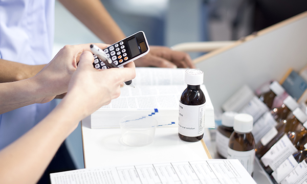 Drug calculations: a nurse using a calculator stands at a desk undertaking calculations for patient medications