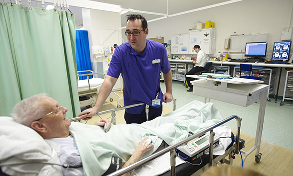 A 2022 study found that 75% of people living with dementia have at least one unplanned hospital admission following diagnosis.  An emergency department nurse keeps a close eye on an older patient lying in a hospital bed