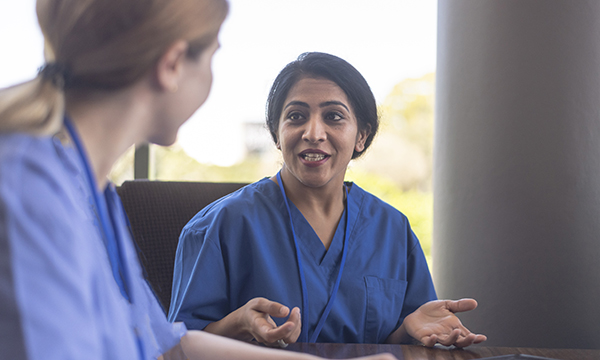 Leading with authenticity builds trust and credibility; a nurse sits and speaks to another nurse, making eye contact and with open palms