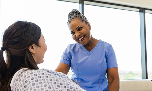 Nurse understaffing on surgical wards has a negative effect on patient recovery; picture shows a nurse smiling at a woman in a hospital gown who is sitting up in a hospital bed