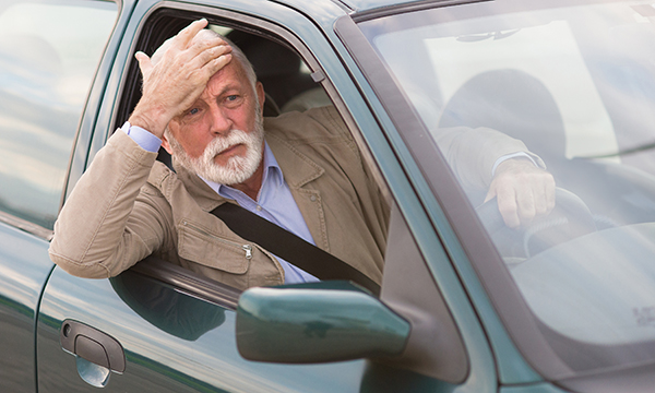 A driver leans out of the window of his car and puts a hand on his brow in confusion. Unsafe driving is an area of risk for accidental self-harm or harm to others.