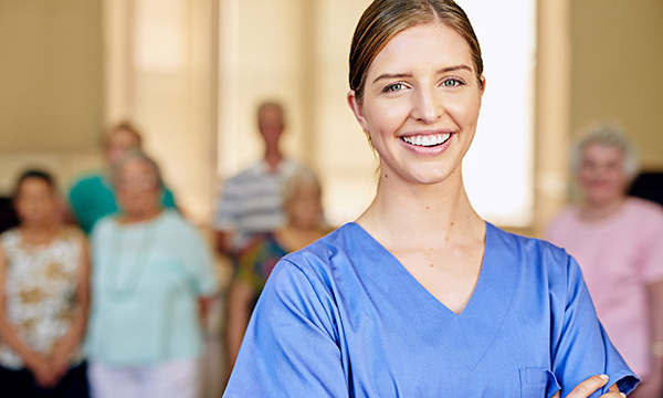 Student acting as nurse in charge in a social care setting: image shows a student in scrubs standing in front of a group of nursing home residents