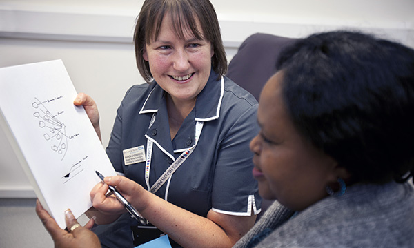 Nurse consultants have a high level of expertise in their area of care; a nurse consultant talks to a patient, explaining something with a smile while showing them a diagram   