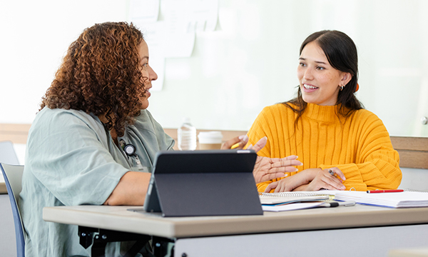 Action plans for nursing students: a student sits at a desk with an instructor, listening as a point is explained