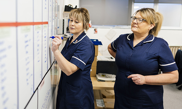 Senior nursing job profiles review: two nurses on shift updating a white board in a staff area
