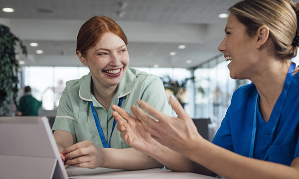 NMC revalidation for nurses: two nurse colleagues laugh together while having a discussion. A reflective discussion is required for revalidation