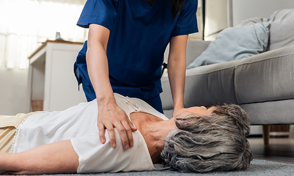 CPR training for nurses: nurse kneels over woman lying on the floor, placing her hands on her shoulders