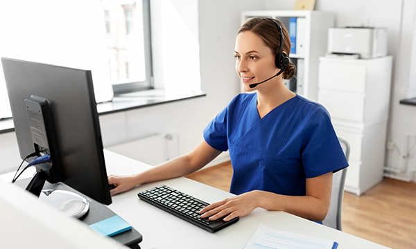 Remote nurse prescribing: a nurse providing patient care remotely sits, wearing a headset with a microphone, as she works on a desktop computer