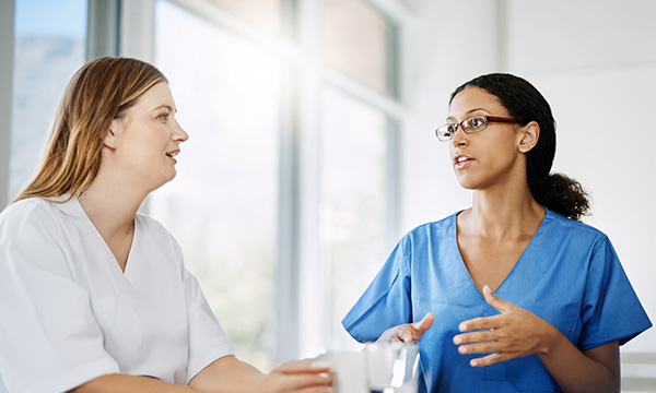Nurse appraisal meeting: two nurses in scrubs sit at a table having a discussion, as in a annual appraisal conversation between a manager and staff member