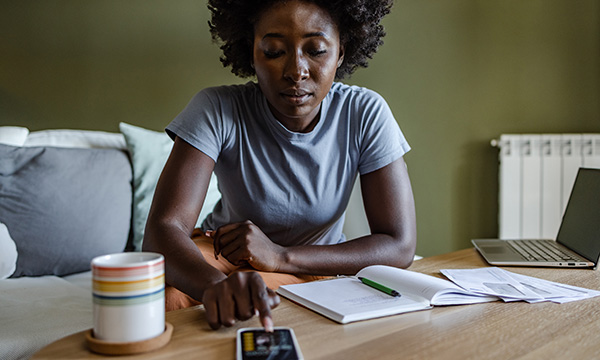 Financial hardship in nursing: a woman sitting at a table with her finger on a calculator key, working out personal living costs