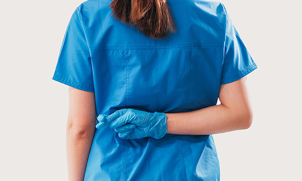 Honest communication with patients: a nurse in scrubs stands with her back to the camera, holding one hand behind her back with her fingers crossed, suggesting not telling the truth