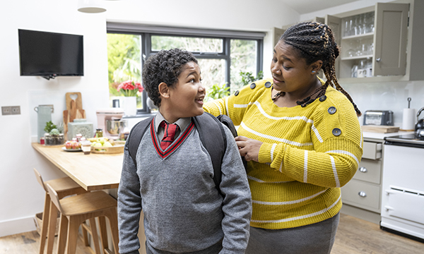 Juggling working and parenting as a nurse: a woman stands in a family kitchen as she helps her son get ready for school
