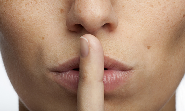 Reporting incidents in nursing: a woman with her finger to her lips, suggesting staff being asked not to speak out about safety incidents