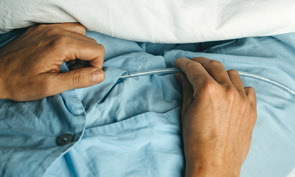 Catheter use and infections: close-up of a patient in pyjamas with their hands resting on top of a urinary catheter tube