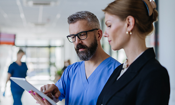 A senior nurse speaks to an NHS manager in a hospital corridor while looking at a tablet