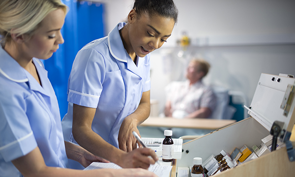 NHS recruitment freezes and newly registered nurses: young nurse and colleague at a ward drugs trolley