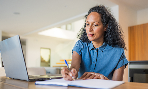 Nurse revalidation: woman works at home on laptop, making notes by hand