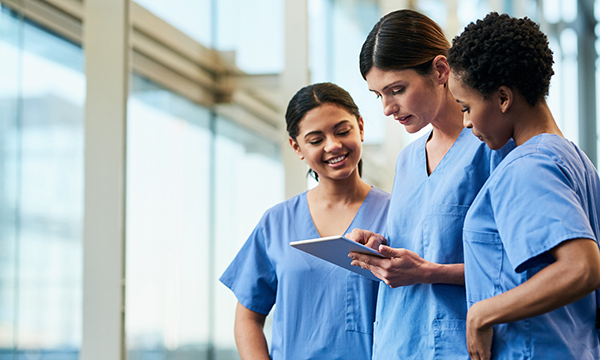 Newly registered nurses: three nurses in discussion in a clinical setting as they look at an electronic pad