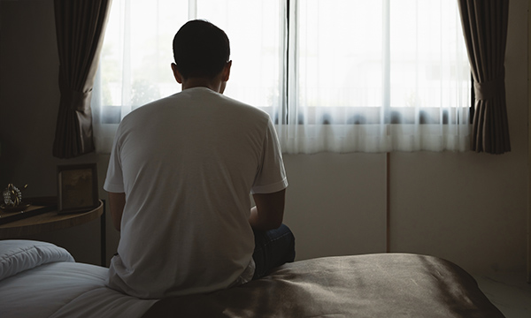 Nurses' suicidal ideation: man viewed from behind sits on bed looking out through window