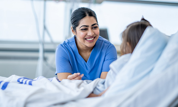Pastoral care in nursing: nurse smiles broadly at bedside of a child in hospital 
