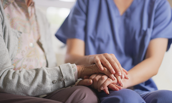 End of life nursing care: a nurse sits beside a patient, holding his hands in hers as a gesture of compassion