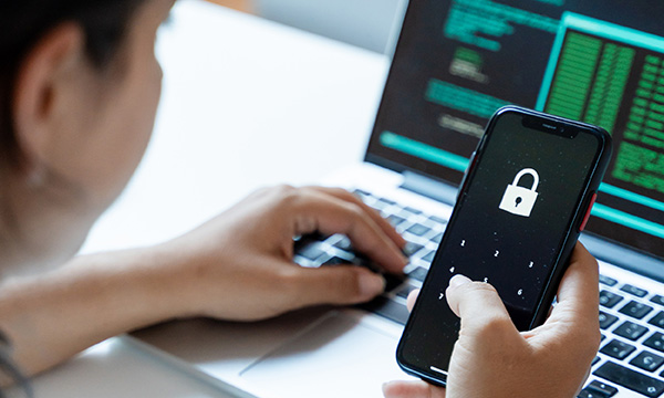 Confidential patient records: a woman looking at files on a laptop and holding a mobile phone in her hand that displays a padlock