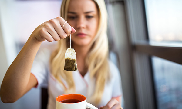 A woman holds a tea bag above a cup of tea