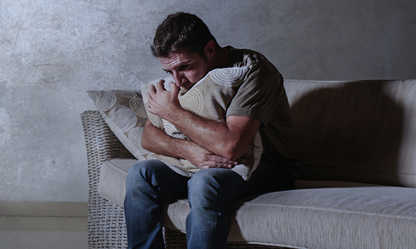An isolated man hugs a pillow on a sofa.&nbsp;Mental healthcare and distress: Lack of nursing experience and confidence to manage distress can lead to a dependence on restraint, seclusion and/or enhanced observations