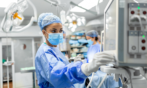 A nurse in scrubs closely monitors a machine during surgery