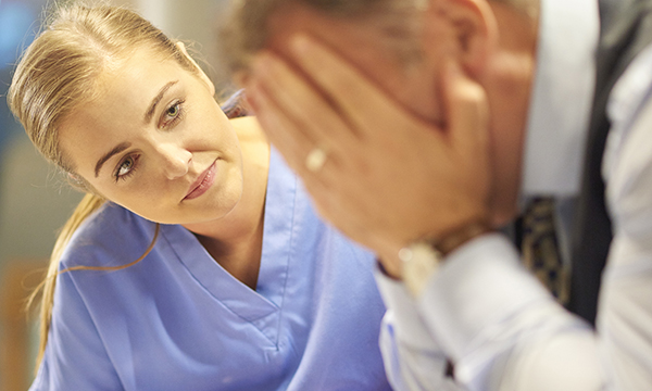 Young female nurse comforts middle aged man with head in his hands