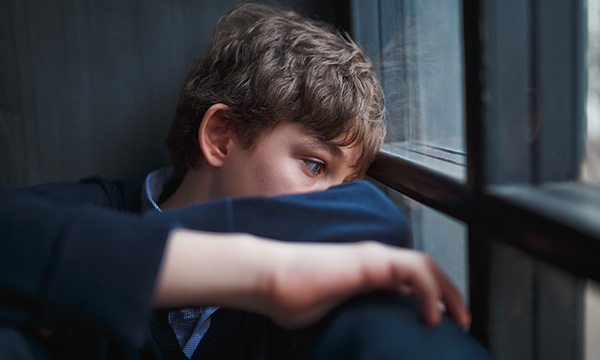 Picture shows a sad looking teenage boy sitting next to a window &nbsp;
