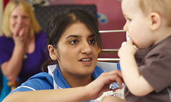 A smiling nurse talks to a young child recovering in hospital as his mother looks on.&nbsp;29% of children in England are living in poverty, fewer are being immunised and there are growing health inequalities with more of the poorest becoming obese
