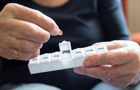 Picture shows older woman taking medication from a dosette box.