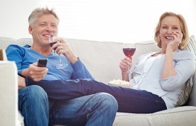 man and woman snuggle on sofa, smiling and drinking wine