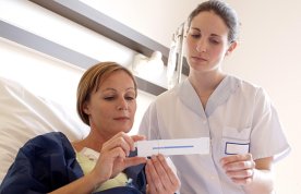 Nursing student stands at bedside assessing patient's pain using pain scale