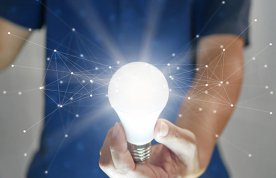 Nurse, face unseen, holds an illuminated lightbulb, with systematically connected dots appearing to radiate from, illustrating the capacity of nurses to be innovative
