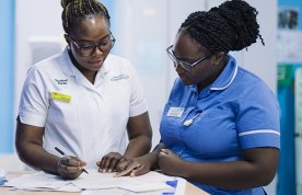 A nursing student stands with a ward nurse as they consult notes together