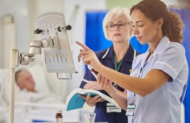 Nursing student or young nurse checks medication at patient’s bedside, while senior nurse checks her work, holding the BNF