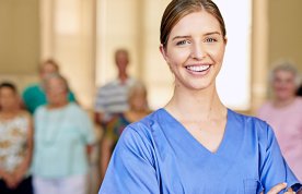 Student acting as nurse in charge in a social care setting: image shows a student in scrubs standing in front of a group of nursing home residents