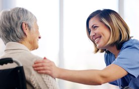 Compassionate dementia care: a smiling nurse places her hand on the shoulder of an older person, who is sitting in a wheelchair