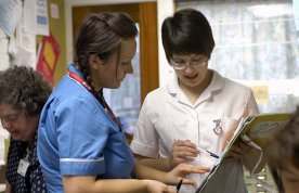 Outdated nursing practice: a nursing student on placement holds a patient’s chart as she asks a senior nurse some questions about it