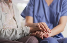 End of life nursing care: a nurse sits beside a patient, holding his hands in hers as a gesture of compassion