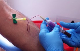 A nurse wearing disposable gloves inserts a needle into a patient’s arm to take a sample of blood