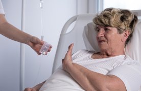 Patient in a hospital bed gestures to refuse her prescribed drugs