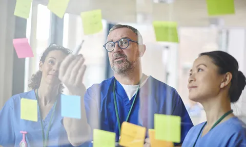Three senior nurses discussing a series of Post-It notes with ideas written on them: good nursing leadership when practising innovation is vital to quality patient care 