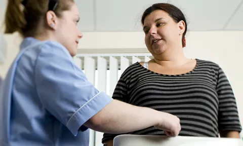 A woman weighs herself on weighing scales while taking to a nurse to the side of her