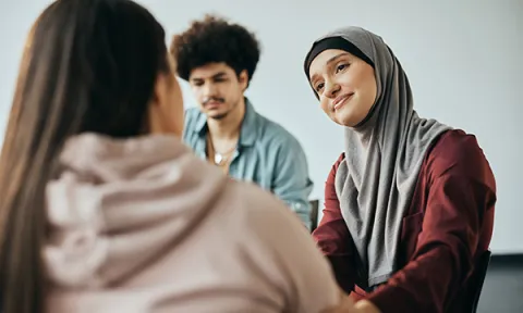 A woman with a compassionate smile sits and looks at another woman who has her back to the camera